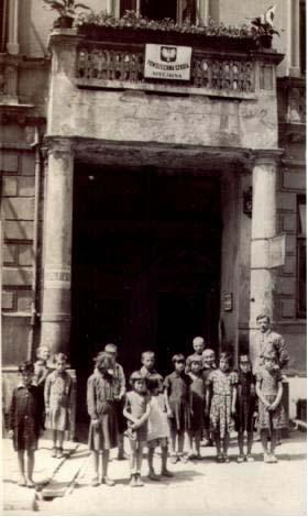 Grupa dzieci przed bramą wejściową do szkoły