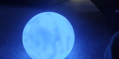zdjęcie ledowej kuli na dywanie, w tle widać rozproszone światło z cotton balls i lekki zarys sylwetki dziecka leżącego z głową na poduszce- relaksuje się