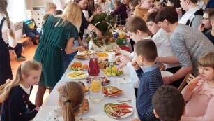 Uczniowie oraz nauczyciele wkoło stołu z jedzeniem.