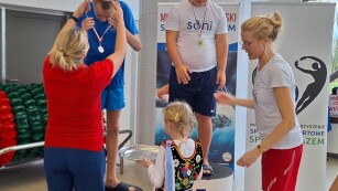 dwóch zawodników dekorowanych przez dwie trenerki i dziewczynka w stroju ludowym podająca medale