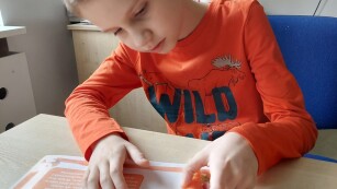 Chłopiec siedzi przy stoliku i trzyma w ręce marchewkę.
