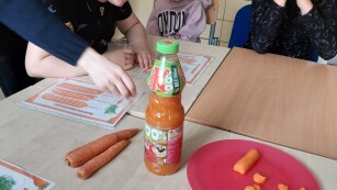 Dzieci siedzą przy stoliku i oglądają przetwory z marchewki.